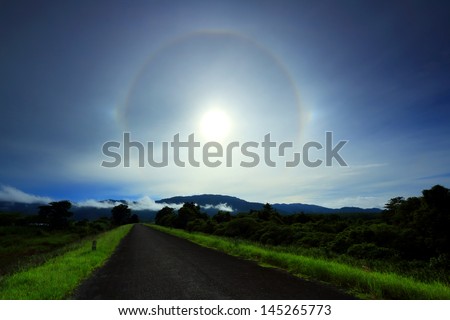 Amazing sun halo above rural road with mountains