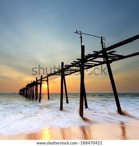 Waves crashing onto the shore and broken wood bridge on sea at sunset