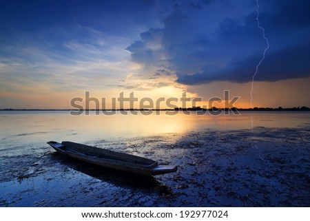 Sunset over small fishing boat with lightning storms in the rainy season on lagoon, Thailand