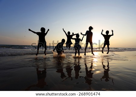 Silhouette of friends of the children jumping on the beach at the sunset time