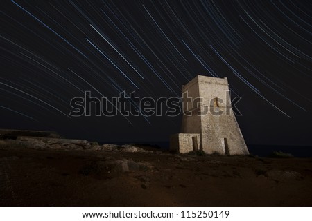 Night shot of a fortification tower in Malta with star trails behind it.