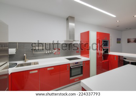Modern gloss red kitchen with a white seamless kitchen top, breakfast bar and stainless steel appliances.