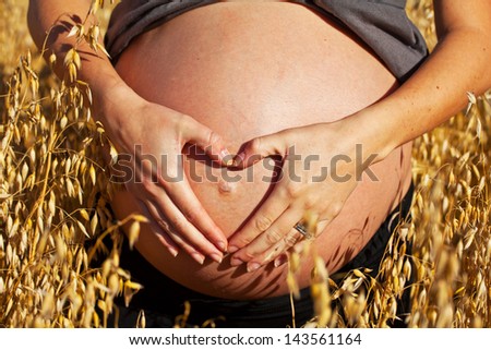a pregnant woman in a field making a heart with her hands over her belly