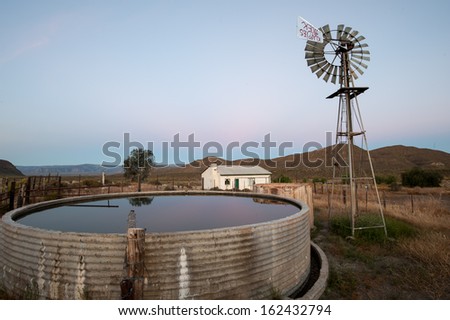 A wind pump, farm building and full concrete water tank in soft light at sunset
