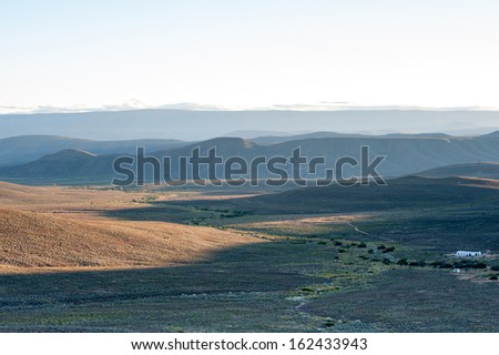 An individual farm house sits in a dark valley at sunrise