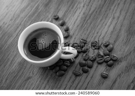 Black and white image of an espresso and coffee beans on a wooden table