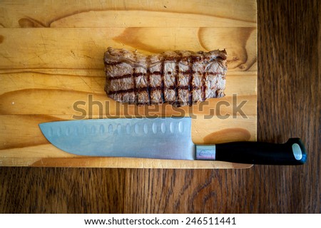 rare beef rump steak and carving knife on a wooden chopping block with a dark wood background