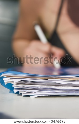 stack of papers in front and pencel in hand in background