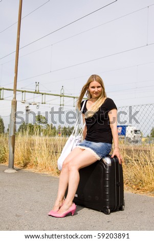 girl sitting on a suitcase waitin for the train or bus