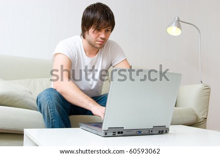young man sitting on sofa at home and working on laptop computer