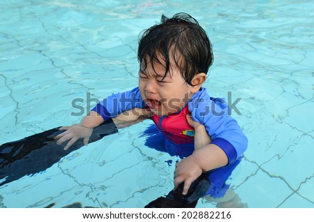 Cute Asian baby girl afraid and crying at her first swimming lesson in a swimming pool