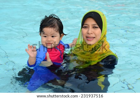 Beautiful young Asian muslim mother enjoying teaching her cute baby girl a first swimming lesson in a swimming pool