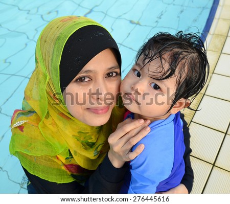 Beautiful young Asian muslim mother enjoying teaching her cute baby girl a first swimming lesson in a swimming pool