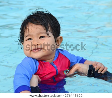 Cute Asian baby girl enjoying and smiling at her first swimming lesson in a swimming pool