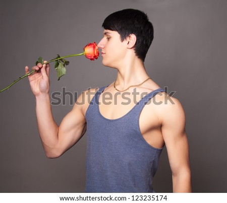 muscular man with red  rose in hands on gray