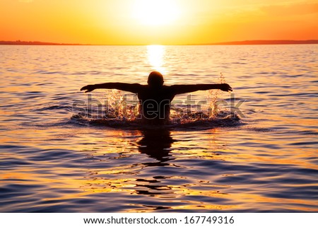 strong young man swiming in the sea over yellow sunrise
