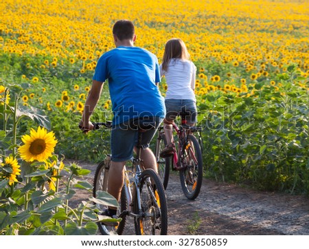 Two happy teen cyclist in sunflower field riding bicycle