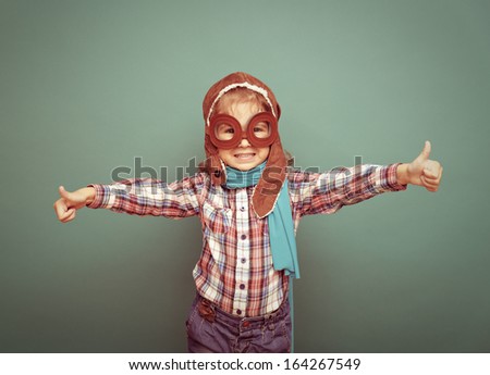 Beautiful happy smiling child (girl)l in helmet on a green background. Vintage pilot (aviator) concept