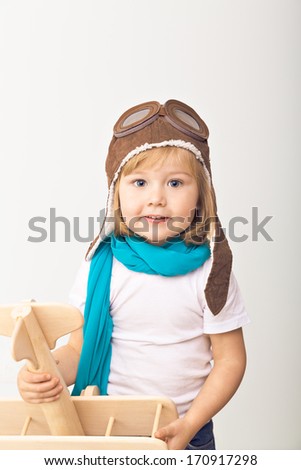 Beautiful smiling child (girl) in helmet on a white background playing with a plane. Vintage pilot (aviator) concept