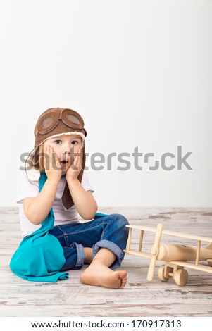 Beautiful smiling child (girl) in helmet on a white background playing with a plane. Vintage pilot (aviator) concept