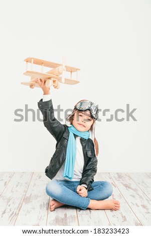 Beautiful smiling child (kid, girl) in helmet on a white background playing with a plane. Vintage pilot (aviator) concept