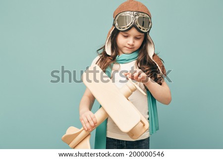 Beautiful smiling child (kid, girl) in helmet on a blue background playing with a plane. Vintage pilot (aviator) concept