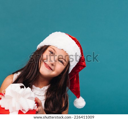 Smiling funny child (kid, girl) in Santa red hat holding Christmas gift in hand. Christmas concept.