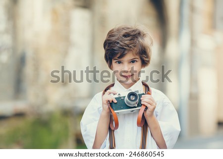 Beautiful smiling child (kid, boy) - photographer  holding a instant camera outdoors