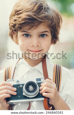 Beautiful smiling child (kid, boy) - photographer  holding a instant camera outdoors