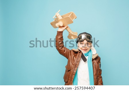 Beautiful smiling child (kid, boy) in helmet on a blue background playing with a plane. Vintage pilot (aviator) concept