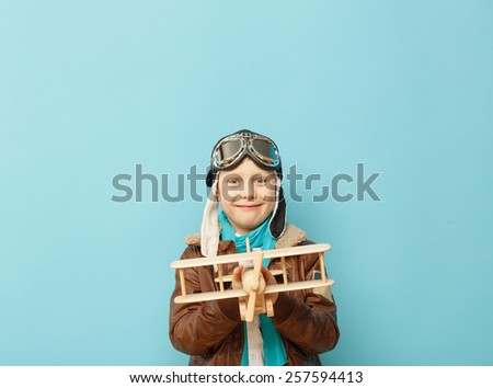 Beautiful smiling child (kid, boy) in helmet on a blue background playing with a plane. Vintage pilot (aviator) concept