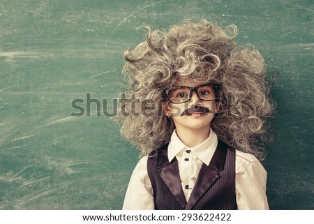 Cheerful smiling little kid (boy) against chalkboard. Looking at camera. Little Einstein style. School concept