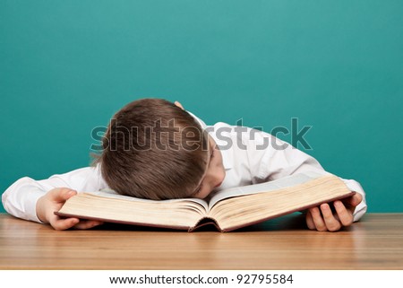 cheerful  little boy sitting at the table  and sleeps on the book. School concept