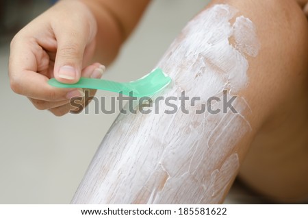 Body hygiene: Woman depilates - scrubs hair removal cream off her leg