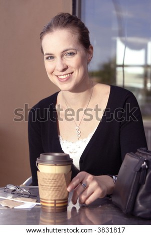 A smiling young woman on cafe patio enjoying a coffee or tea.