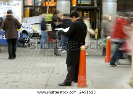 Man reading newspaper amidst evening bustle of London\'s Chinatown, shot on slow shutter speed.