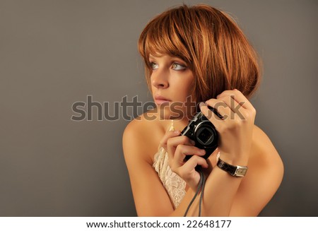 Portrait of a beautiful redhead holding compact camera on gray background.