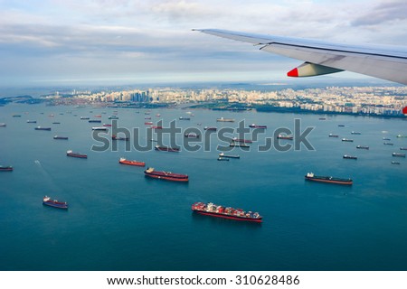 Bird\'s-eye view seascape with cargo ship in the morning from window of airplane with cityscape background.