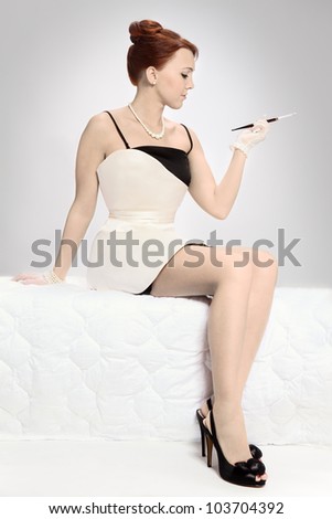 Young pensive woman in style of sixties  dreaming of something and smoking on the bed