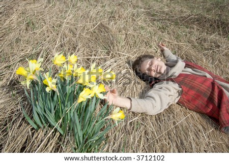 Woman lying at field of dry herbage near yellows narcissi