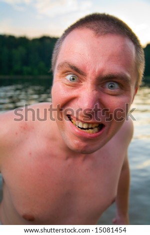 Crazy man with bad yellow teeth making face  near river at evening.