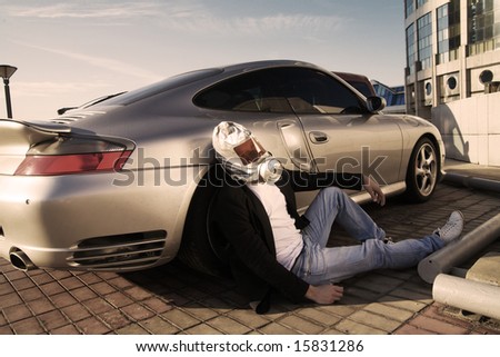 Sick man in gas mask sitting near expensive car at parking in the city