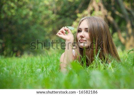 Young beautiful woman lying at grass and looking at blade of grass in her hand
