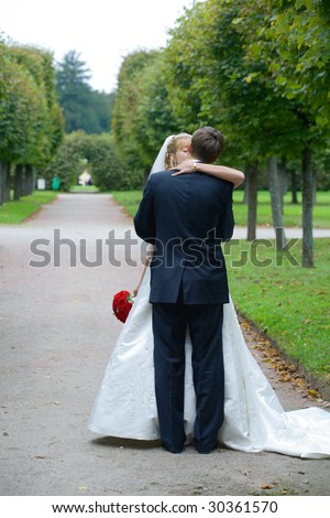 Full-length picture of kissing on the path in the park, the groom is standing with his back to the camera