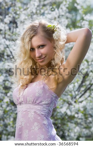 Attractive young lady standing near blooming cherry tree and smiling