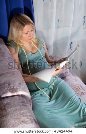 Pregnant woman sitting at sofa and reading some journal