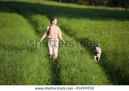 50 years old woman walking with alsatian dog at summer field