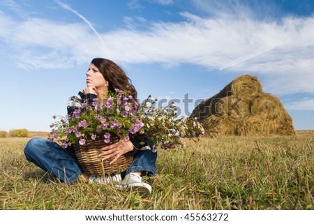 Young beautiful woman with basket of flowers sitting at autumn field