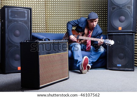 Guitar player in recording studio at sofa with guitar amplifier and audio systems