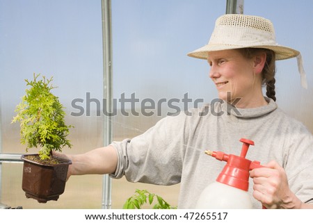 Middle aged smiling woman watering plant in her hands